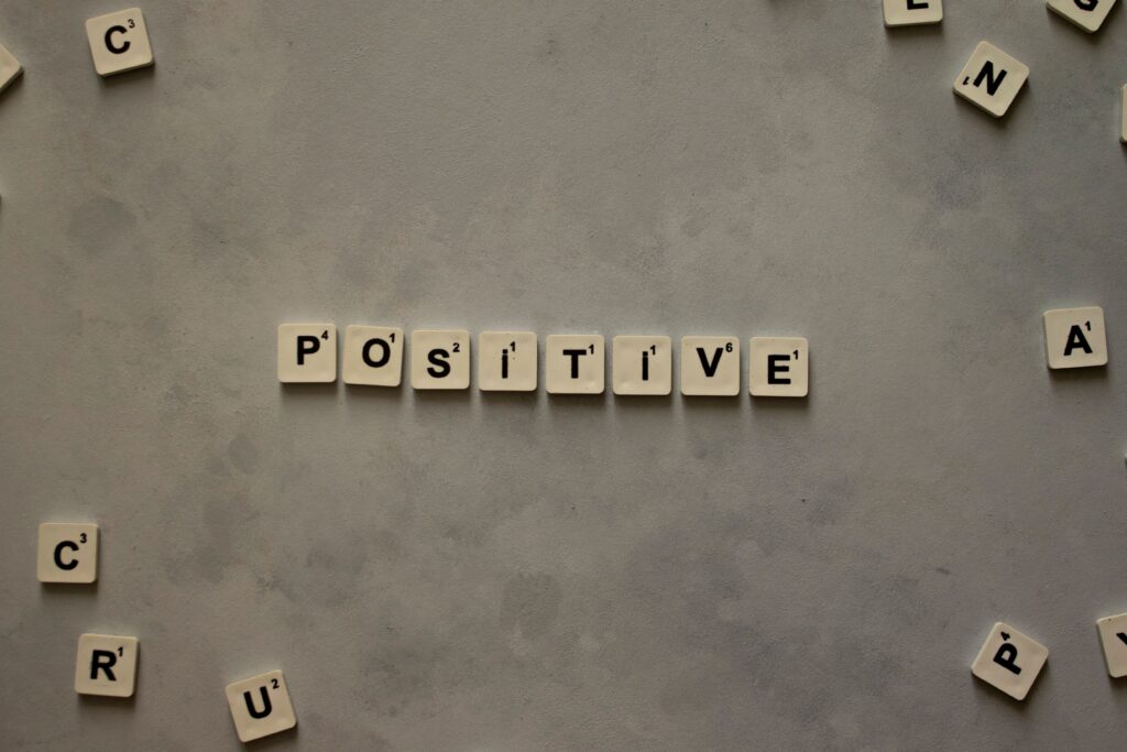 Scrabble tiles arranged to spell 'positive' on a gray textured surface, conveying optimism.