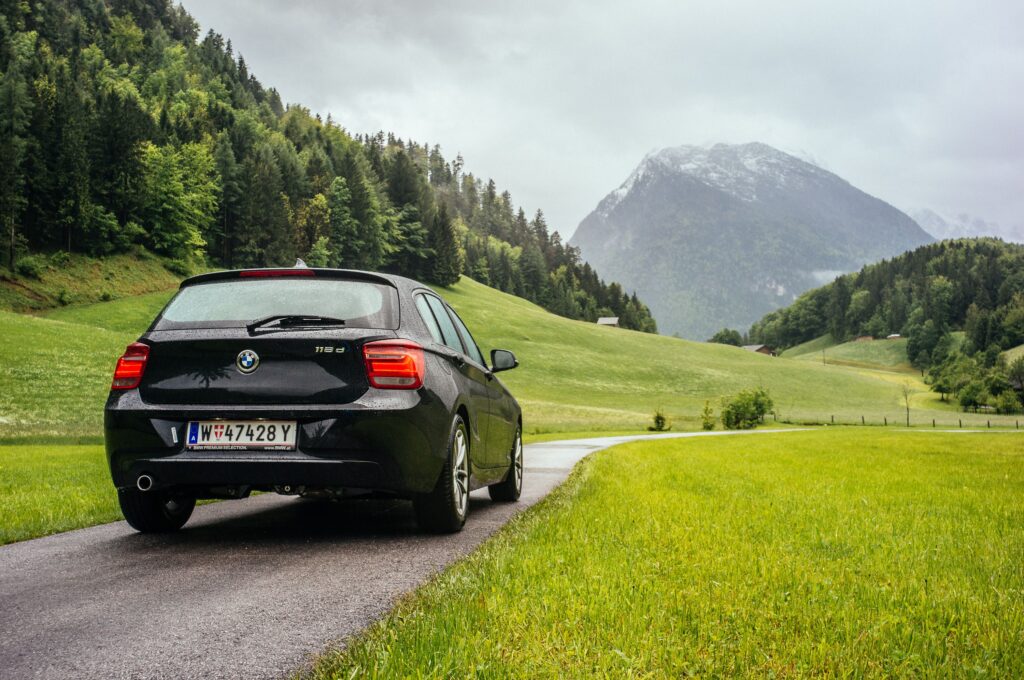A BMW Series 1 drives on a country road in Salzburg, Austria, surrounded by lush fields and mountains.