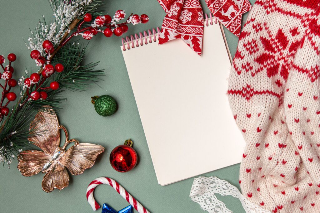 From above of empty spiral notebook with warm knitted sweater composed with various Christmas decorations and candy cane